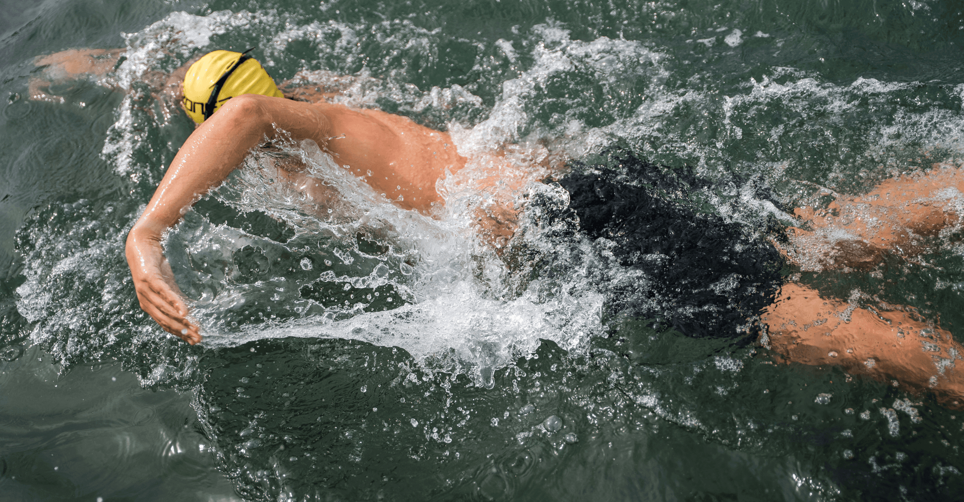 Swimmer wearing a yellow cap and goggles glides through water during a training session.