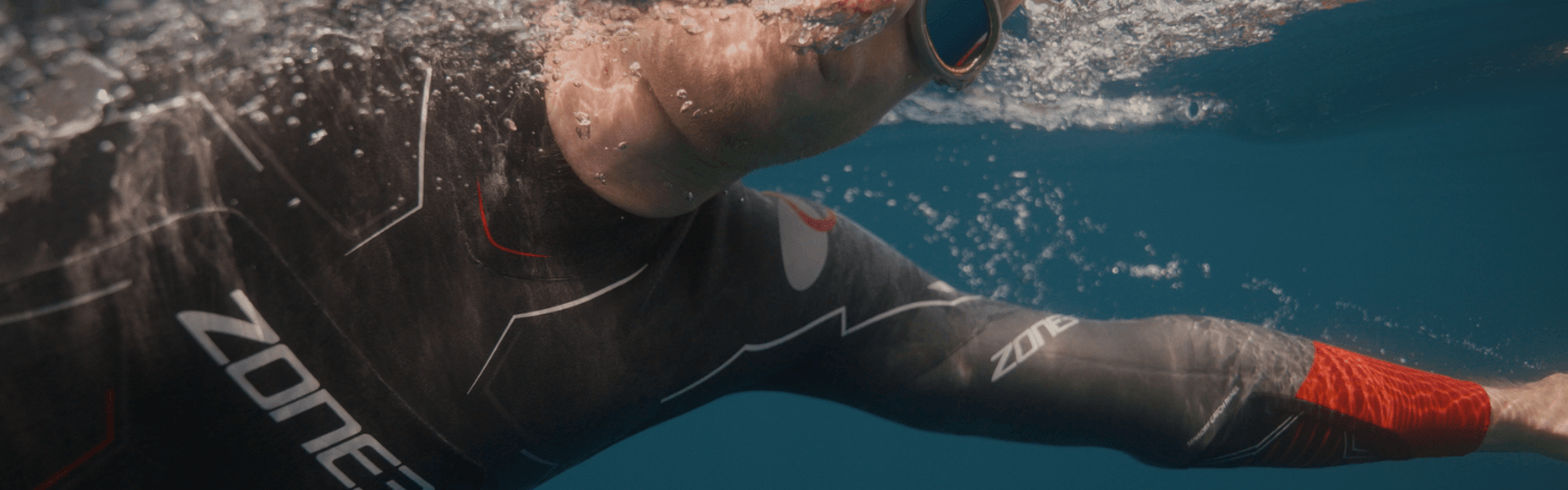 A person is swimming in the sea in a ZONE3 wetsuit and breathing to one side