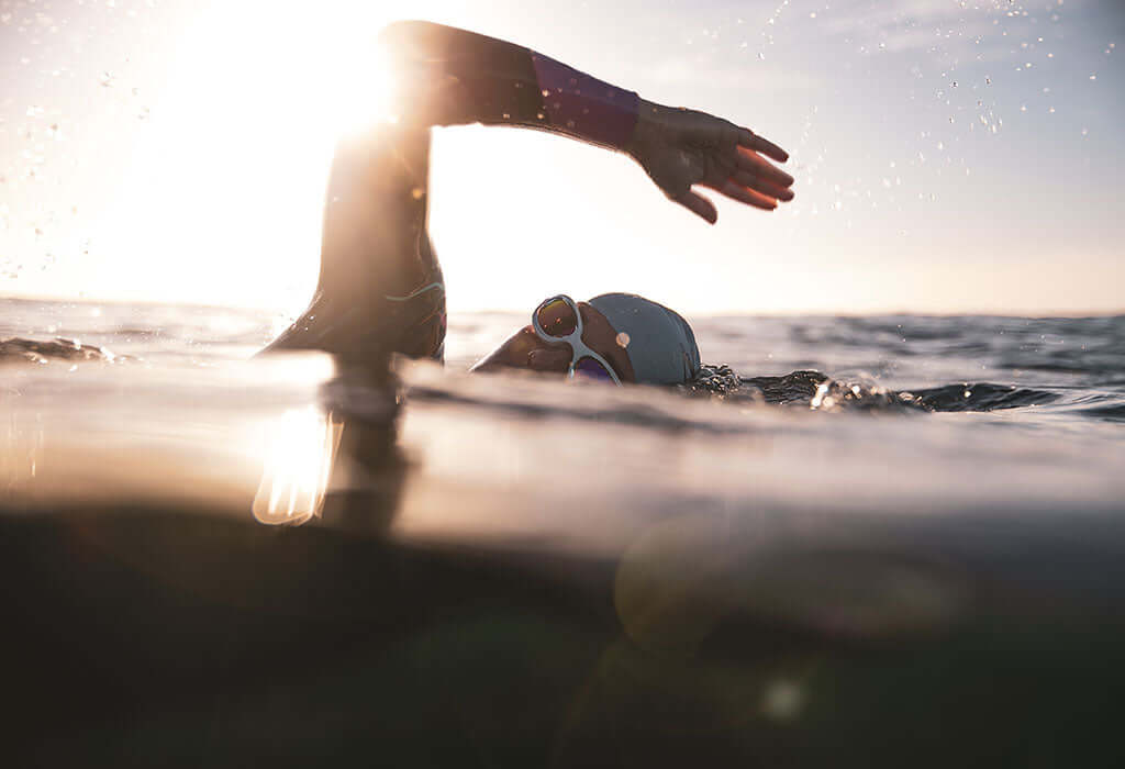 Open water swimmer wearing a cap and goggles glides through sunlit tidal water