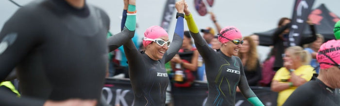 two women who are part of the triathlon group '10Ironwomen are running into the water at the start of an Ironman race - they are holding hands above their heads