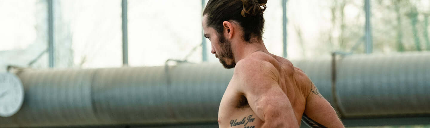 Shirtless male swimmer with a tattoo warming up in an indoor training facility