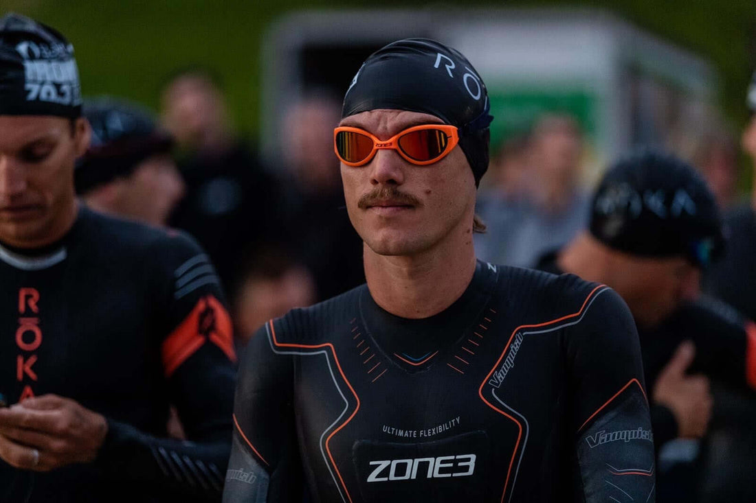 Male athlete in a black Zone3 wetsuit and orange sunglasses at a race start among fellow competitors