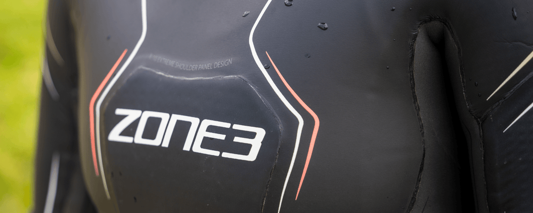 Close-up of a Zone3 triathlon wetsuit with white and red piping and water droplets on dark neoprene.