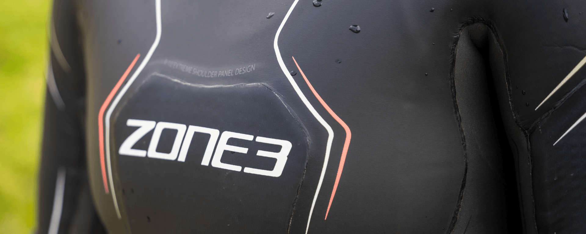 Close-up of a Zone3 triathlon wetsuit with white and red piping and water droplets on dark neoprene.