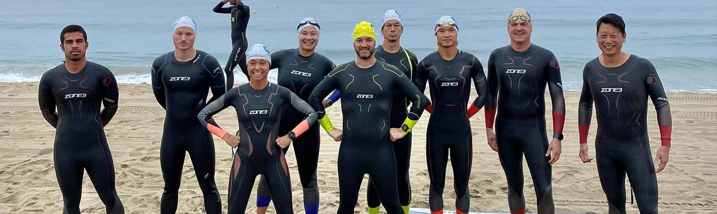 Group of Zone3 wetsuit swimmers posing on a sandy beach before an open water session