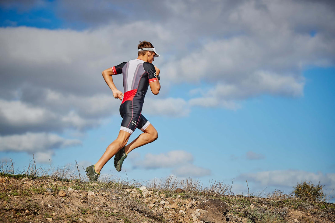 Triathlete runs uphill on a rocky trail with dark clouds and blue sky overhead