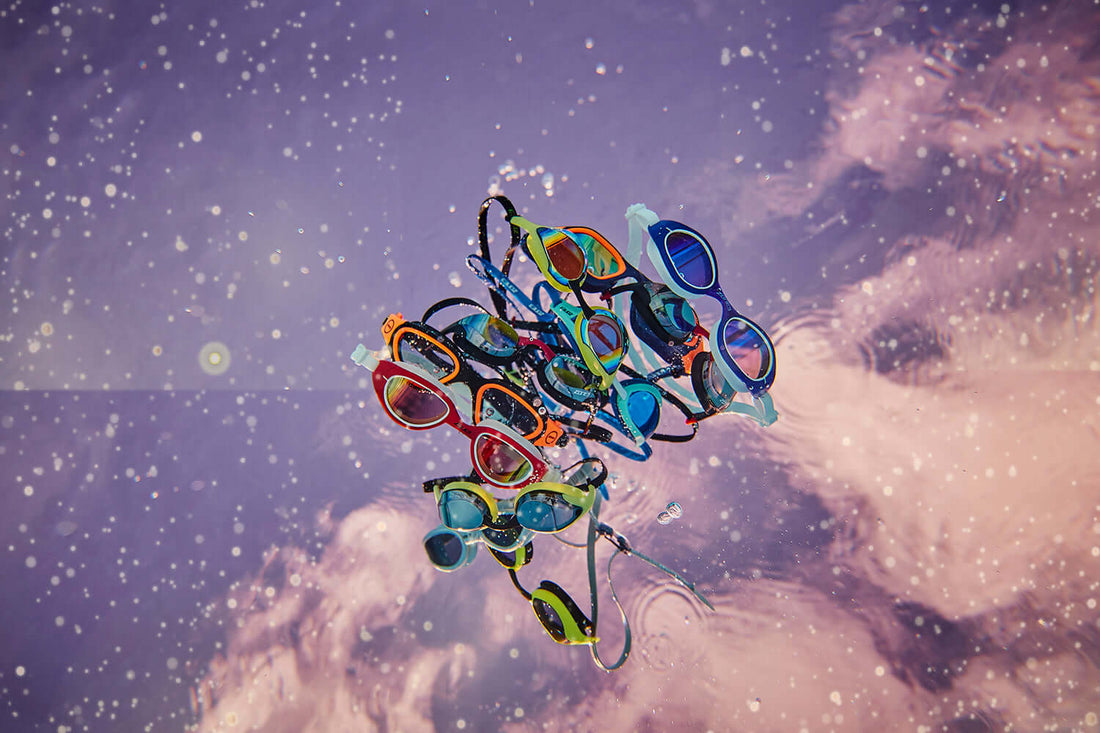 Group of colorful swimming goggles floating underwater against a purple background.