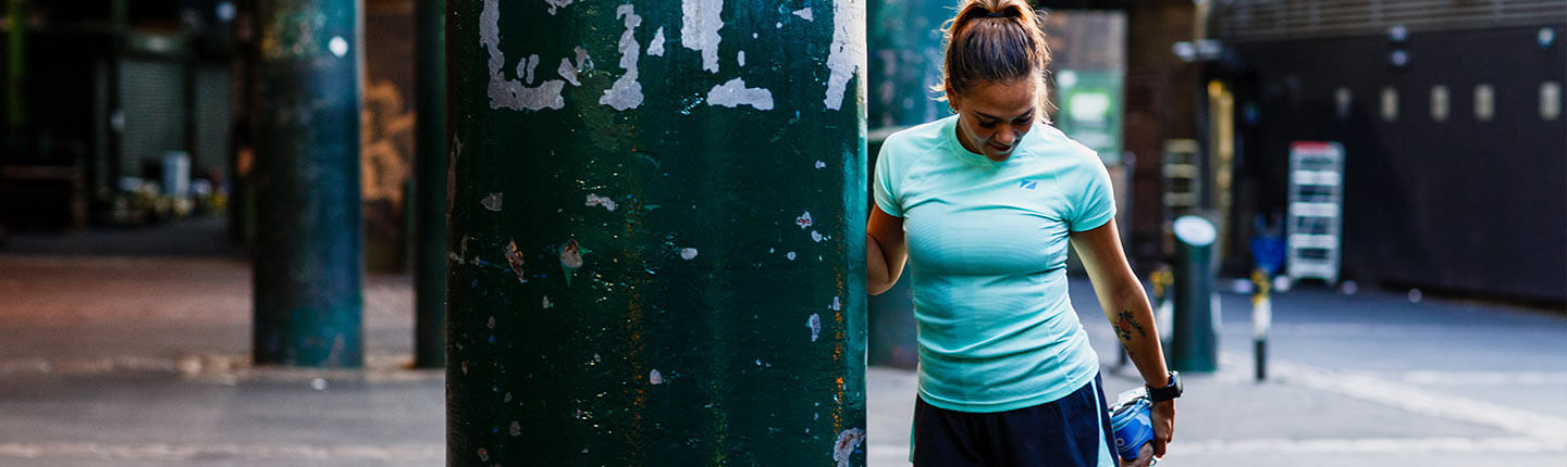 Runner in turquoise top leans on a street pillar during hot weather training in the city