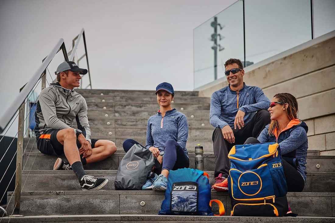 Four athletes in matching blue gear sit on outdoor stadium stairs chatting.