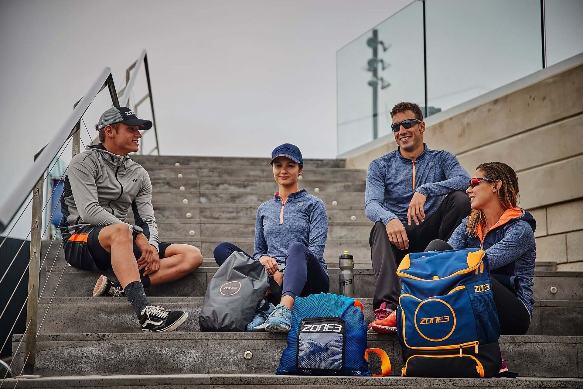 Four athletes in matching blue gear sit on outdoor stadium stairs chatting.