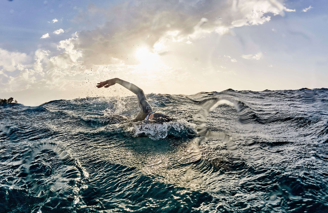 Swimmer in rough ocean with one arm extended above choppy water and sun breaking through clouds