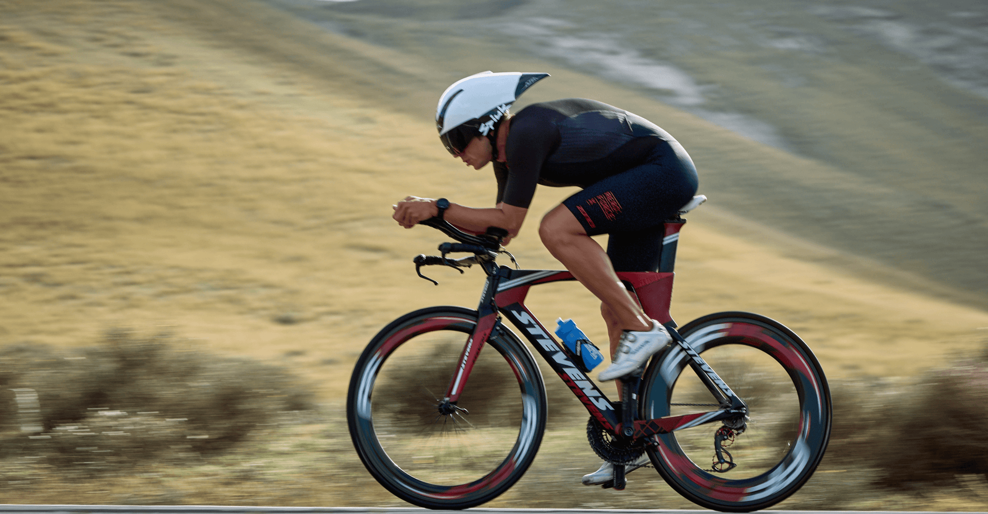 Triathlete riding a time trial bike in an aerodynamic forward position wearing a white aero helmet