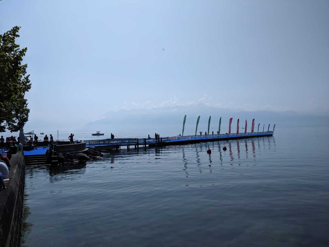 Lakeside race pier extends into calm water with colorful flags along the railing and spectators along the shore