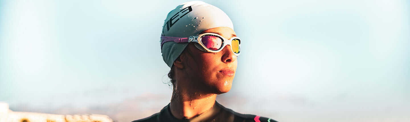 Close up of a swimmer wearing a white cap and goggles gazing toward the horizon over the water.