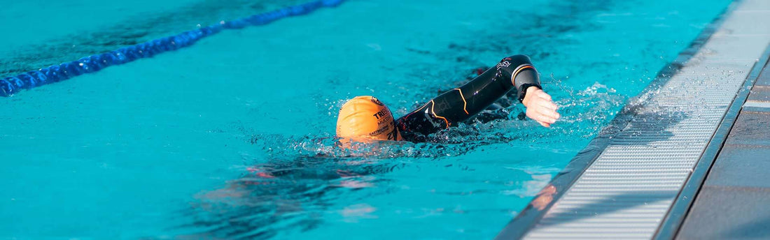 Swimmer wearing an orange cap trains laps in a turquoise pool with a lane rope