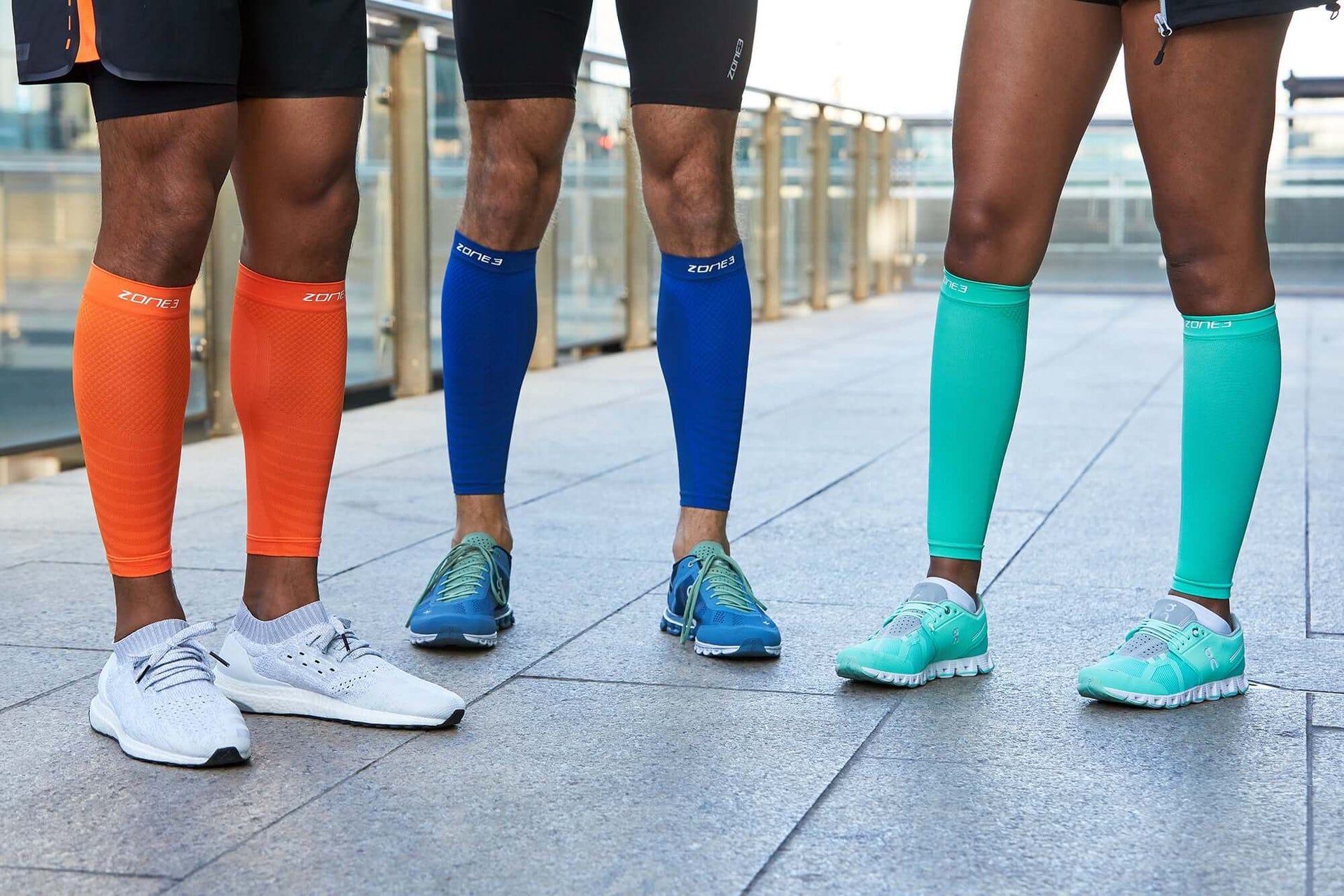 Group of runners wearing bright Zone3 compression calf sleeves in orange blue and teal on a track