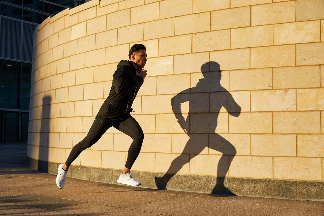 Runner in a black jacket sprints past a curved stone wall during golden hour.