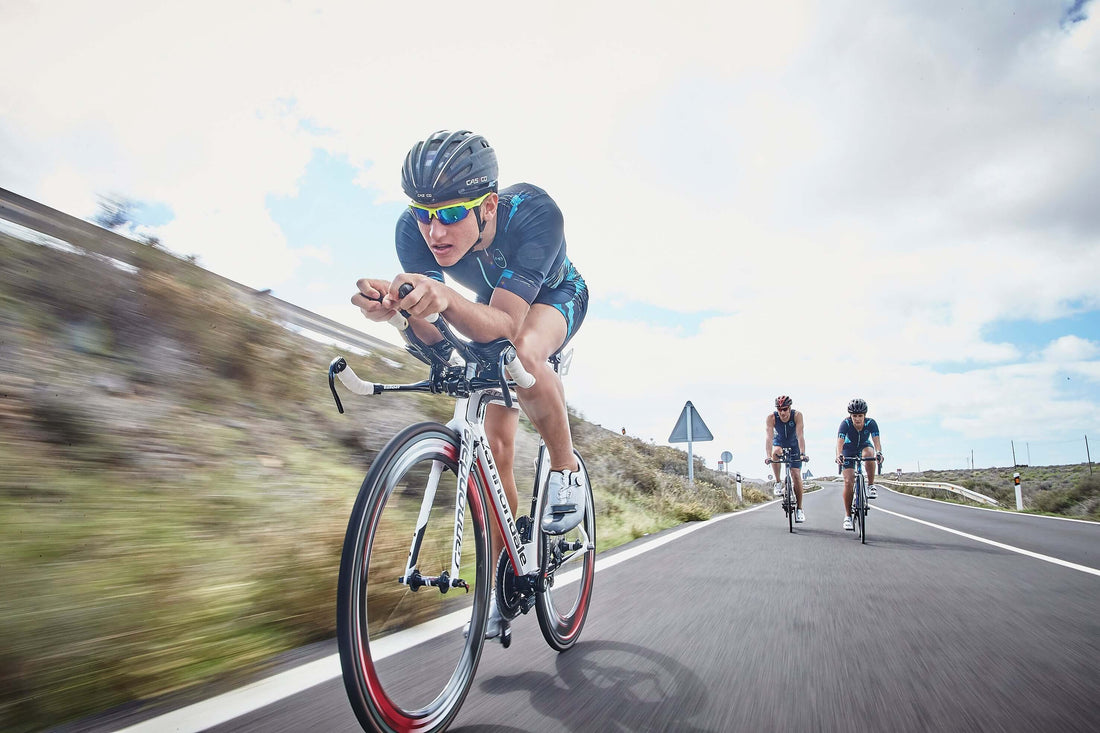 Road cyclist in aero helmet and blue kit leans forward on a fast group ride with other riders behind