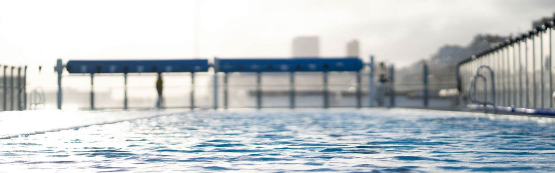 Low angle view over a swimming pool surface with blue water and a blurred pool deck in the background.