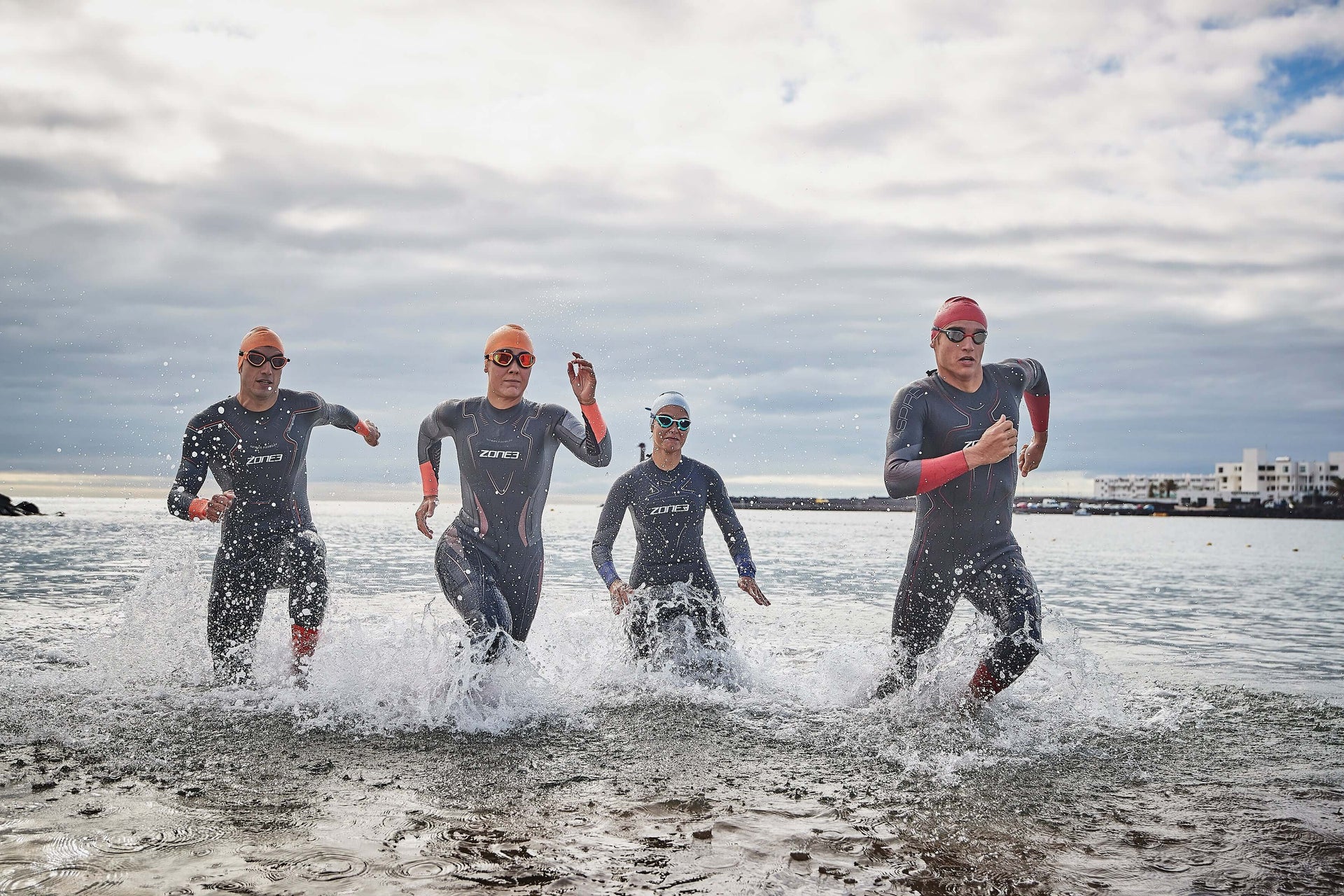 Triathletes in wetsuits sprinting out of the water during an open water start with spray around their legs.