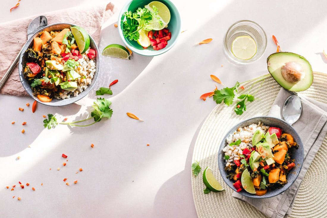 Vegan rice bowl with avocado cubes peppers cilantro and a lime wedge on a light surface
