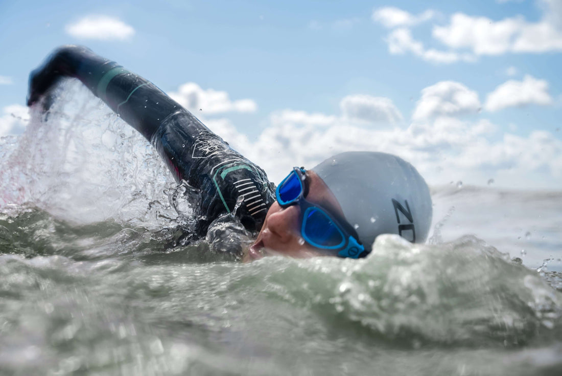 Triathlete in a wetsuit with blue goggles powers through choppy water under a clear sky.