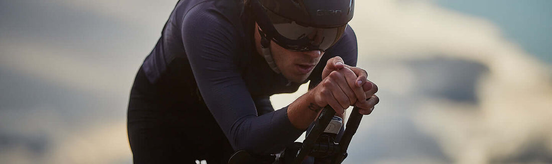 Cyclist in aero position wearing helmet and dark kit gripping aero handlebars