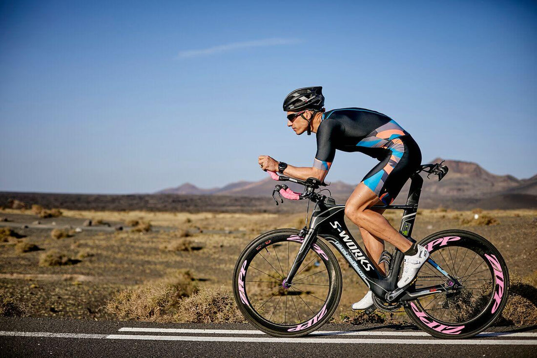 Cyclist in aero helmet and colorful kit rides a black S-Works time trial bike on a desert road.