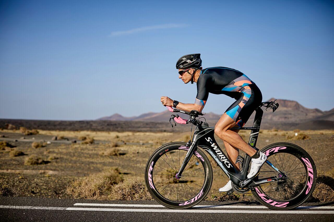 Cyclist in aero helmet and colorful kit rides a black S-Works time trial bike on a desert road.