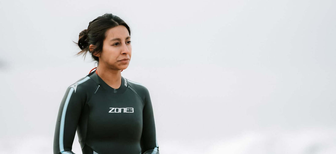 Woman in a Zone3 wetsuit stands by the sea looking ahead toward the horizon.