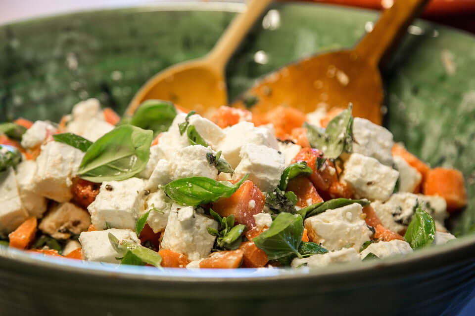 Gluten free salad with feta cheese cubes tomatoes and fresh basil in a green bowl