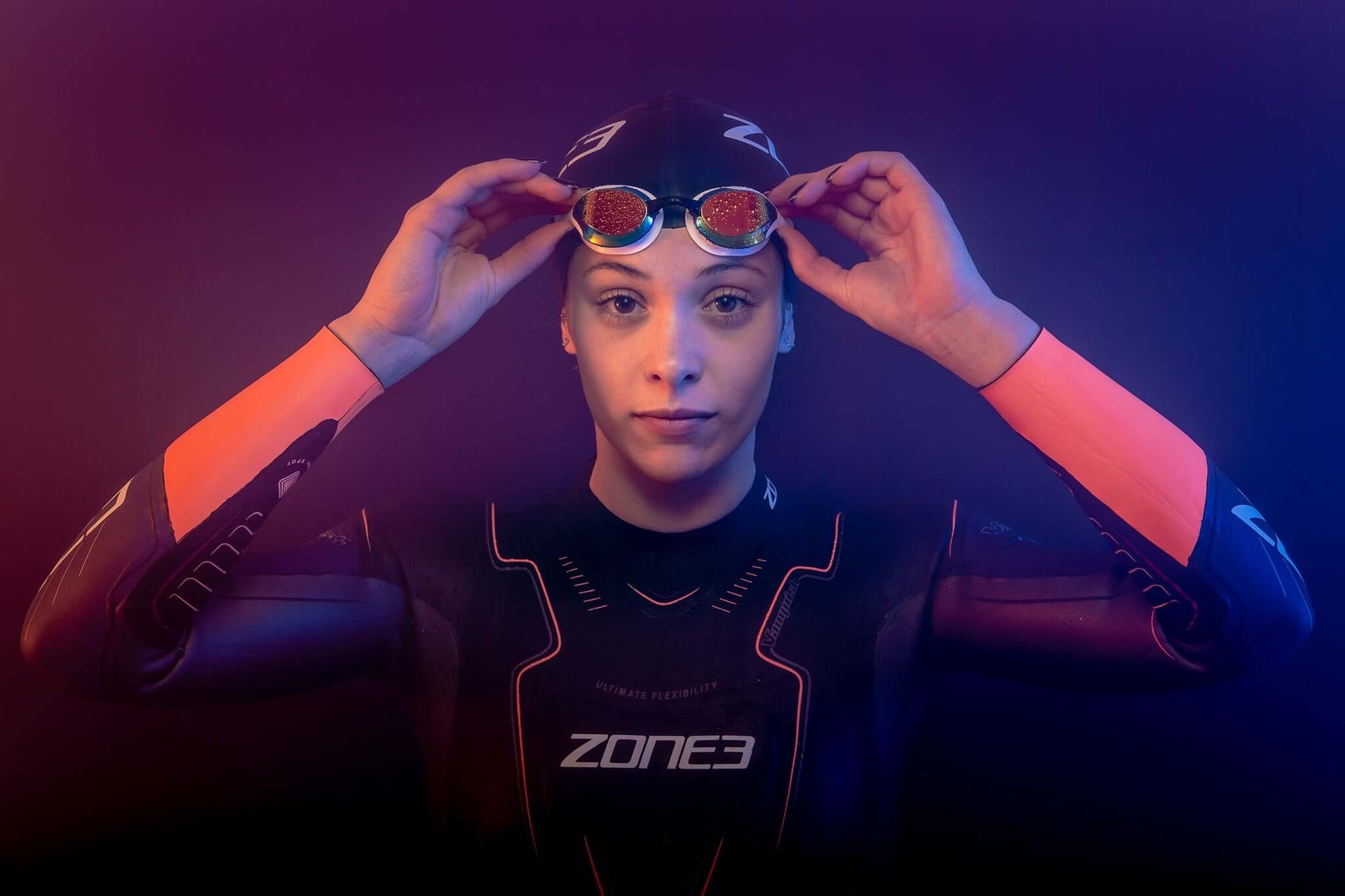 Portrait of a Zone3 athlete in a black wetsuit adjusting goggles against a purple gradient background