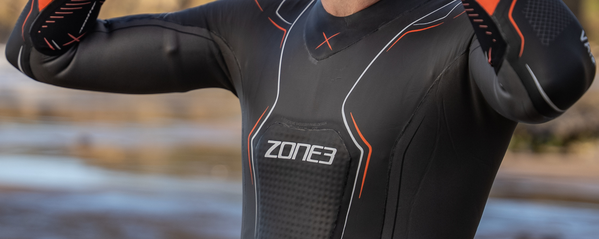 Close up of a black Zone3 wetsuit with white and orange piping and the Zone3 logo on the chest.