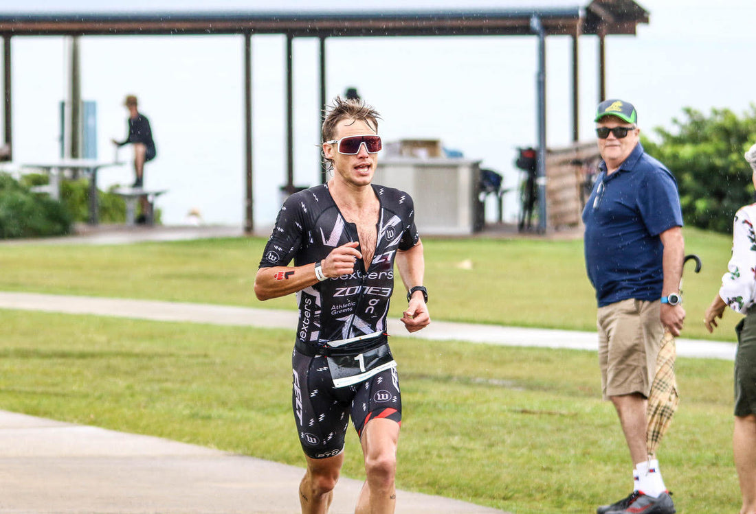 Triathlete in a black racing suit runs on a course with spectators in the background