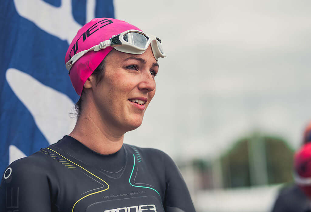 Close up of a female triathlete in a pink swim cap and goggles looking ahead.