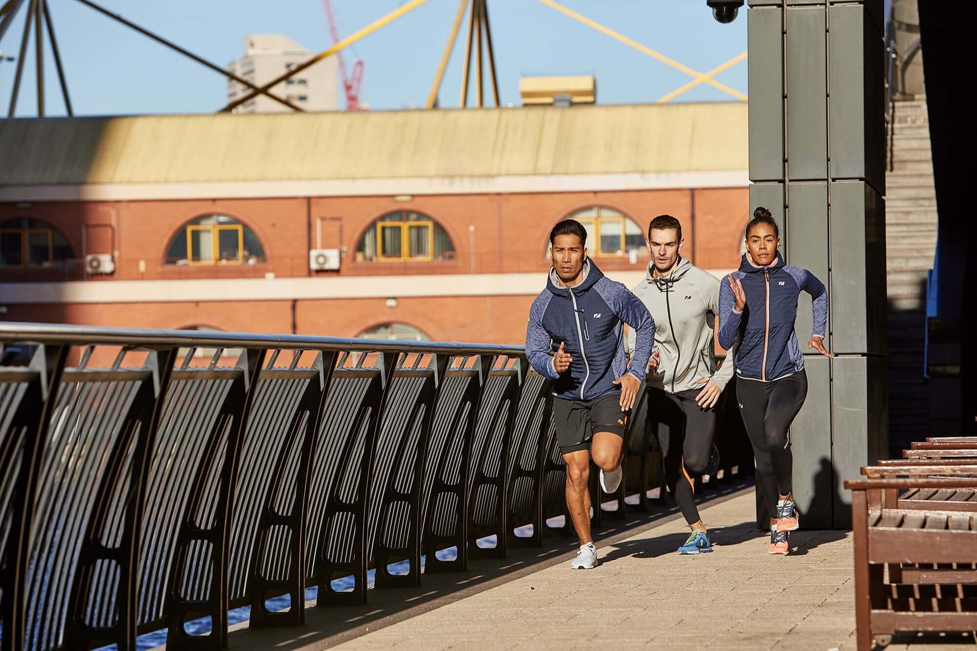 Three Zone3 athletes in RX3 compression gear run along a sunlit urban bridge.