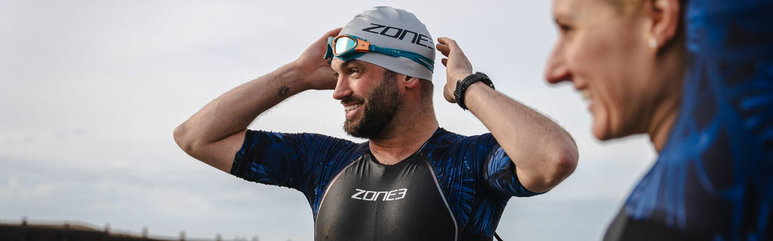 A man is looking in the distance, wearing ZONE3 kit, goggles and cap