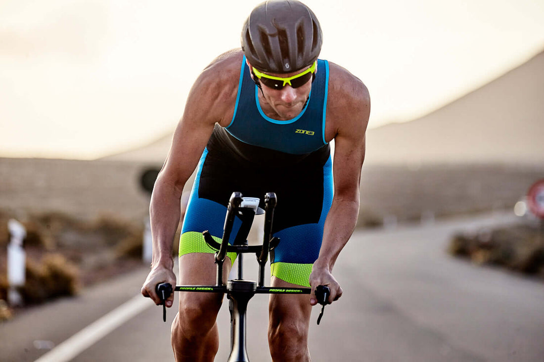 Triathlete in blue kit and aero helmet crouches over a time trial bike on an open road.