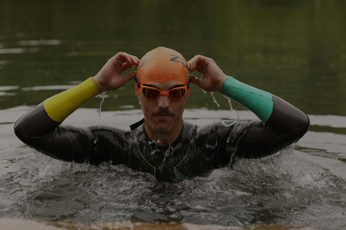 Swimmer wearing an orange cap and orange goggles adjusts the goggles while emerging from open water