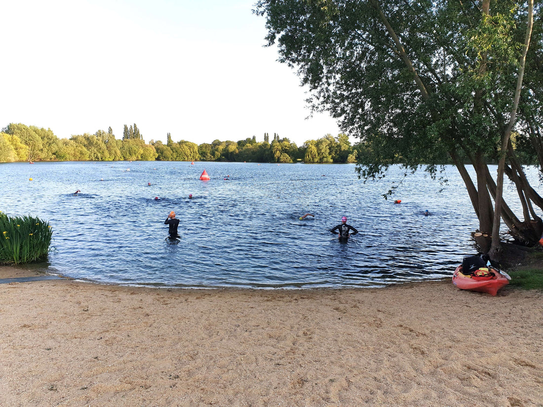 Swimmers in a lake during open water training with buoys marking the course and a tree lined shore in the background.