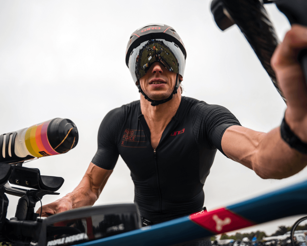 Triathlete in black race kit and aero helmet with mirrored visor racing outdoors on an aero bike