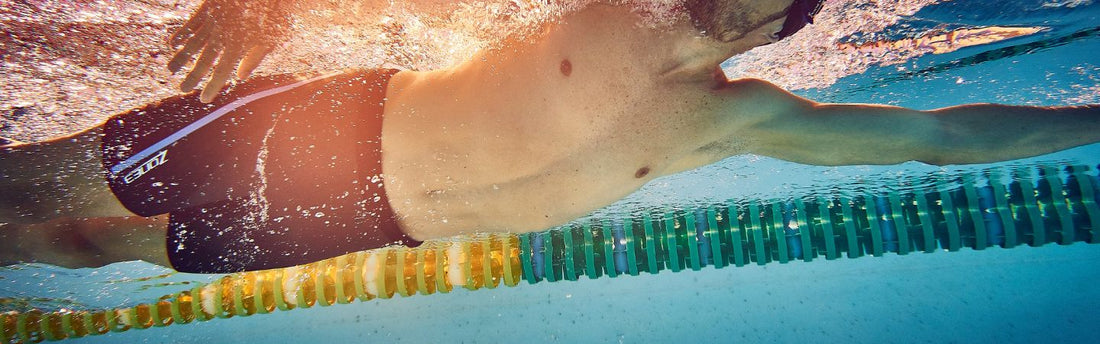a man is swimming in the pool wearing buoyancy shorts the photo is taken from under the water with the person swimming above
