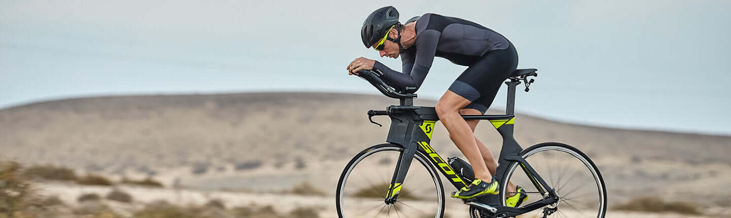 Cyclist in aero position on a Scott time trial bike riding through a desert landscape.