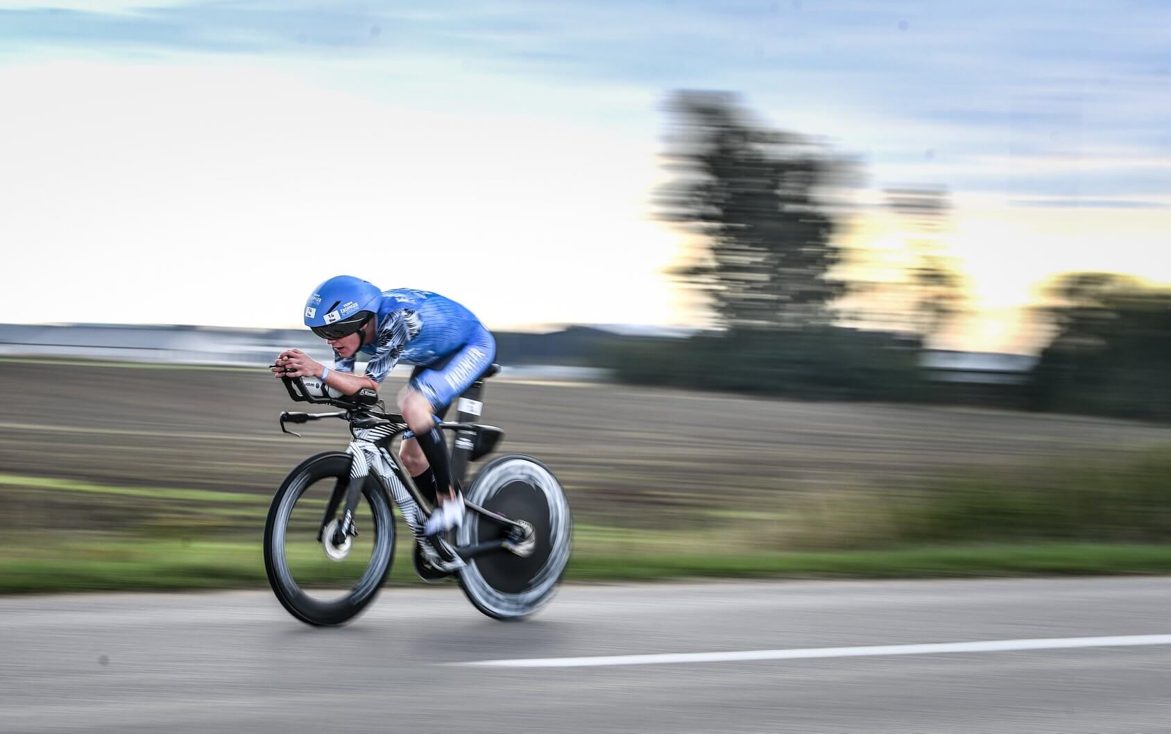 Triathlete in blue aero kit rides a time trial bike with a disc rear wheel during a road race