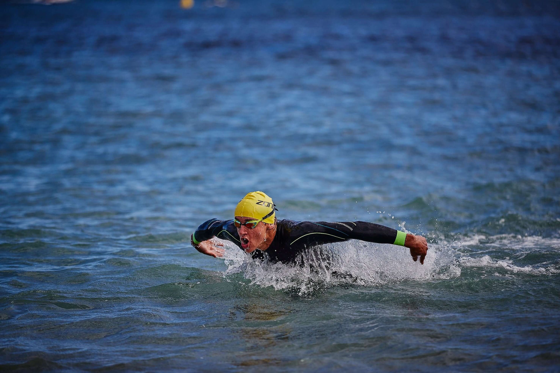 Open water swimmer in a black wetsuit and yellow cap gliding through blue waves