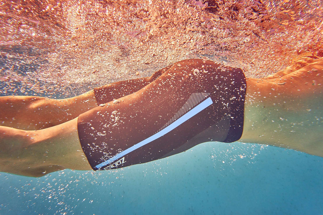 Underwater view of a swimmer wearing buoyancy shorts with a light stripe as bubbles rise around.