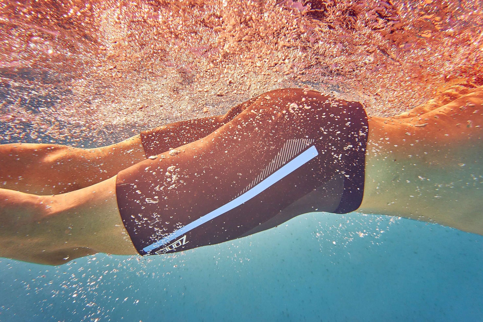 Underwater view of a swimmer wearing buoyancy shorts with a light stripe as bubbles rise around.