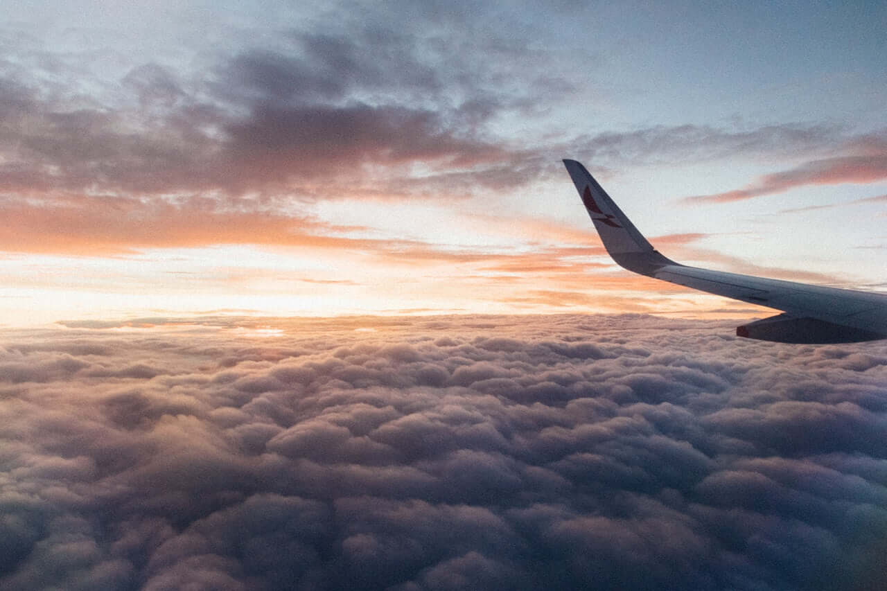 Airplane wing in sunrise light with clouds below and the wingtip visible.