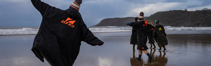 A group of swimmers are running on the sand at low tide towards the water - they are wearing zone3 changing robes to keep warm.