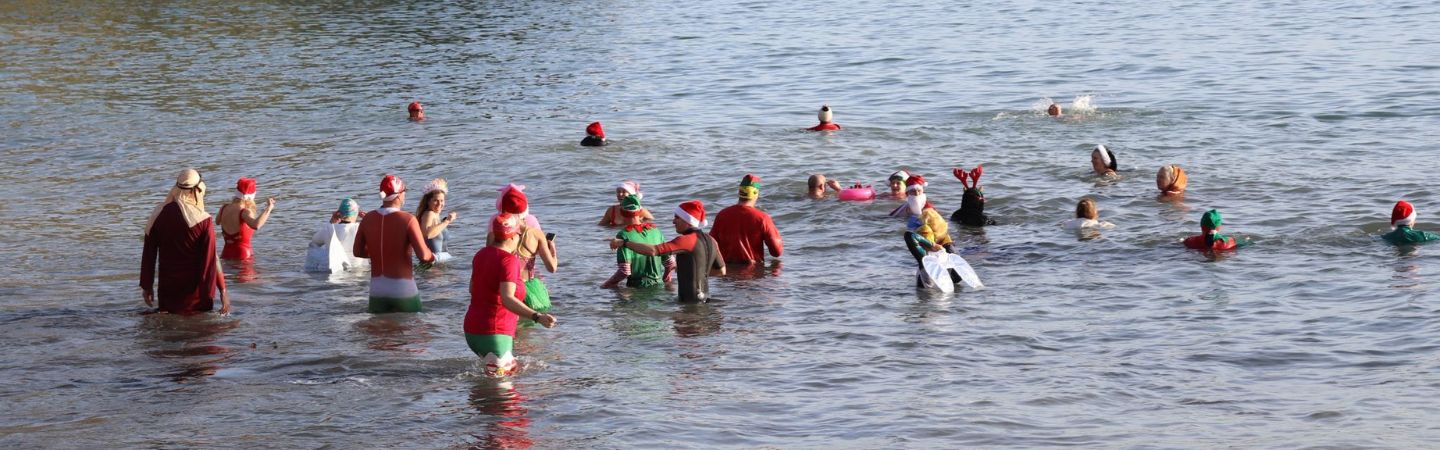 a group of people are in the sea for a cold water swim and festive swim, wearing festive outfits